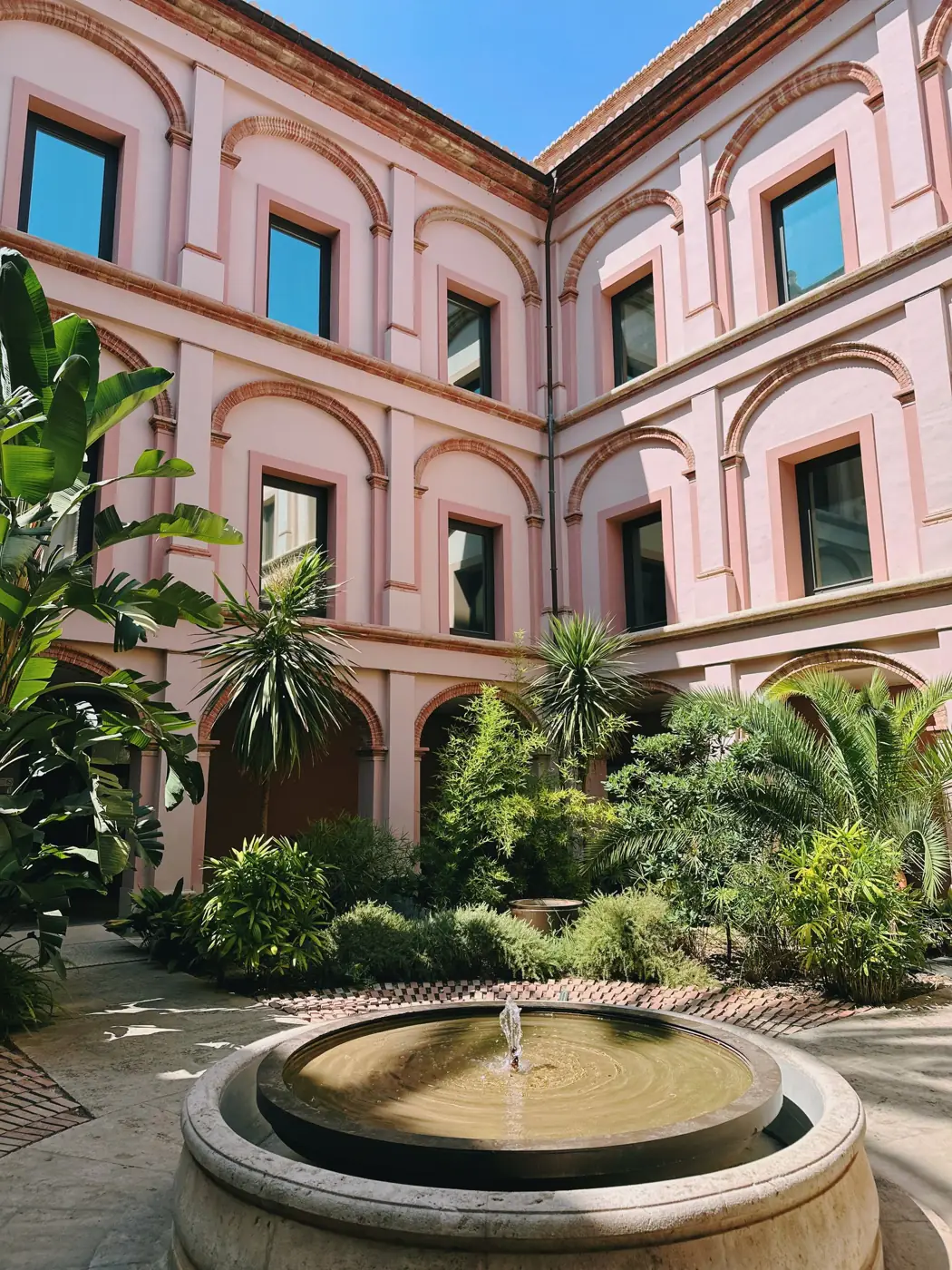 Enclosed courtyard garden with a stone fountain, palms and lush green planting