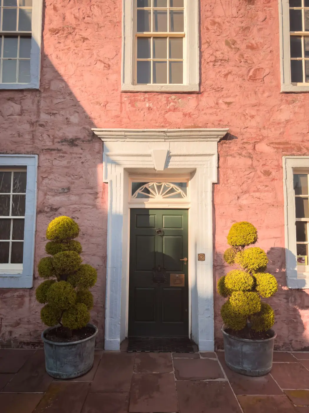 Period town house entrance flanked by clipped topiary in terracotta pots